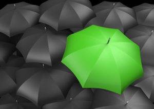 one green umbrella amongst many black ones